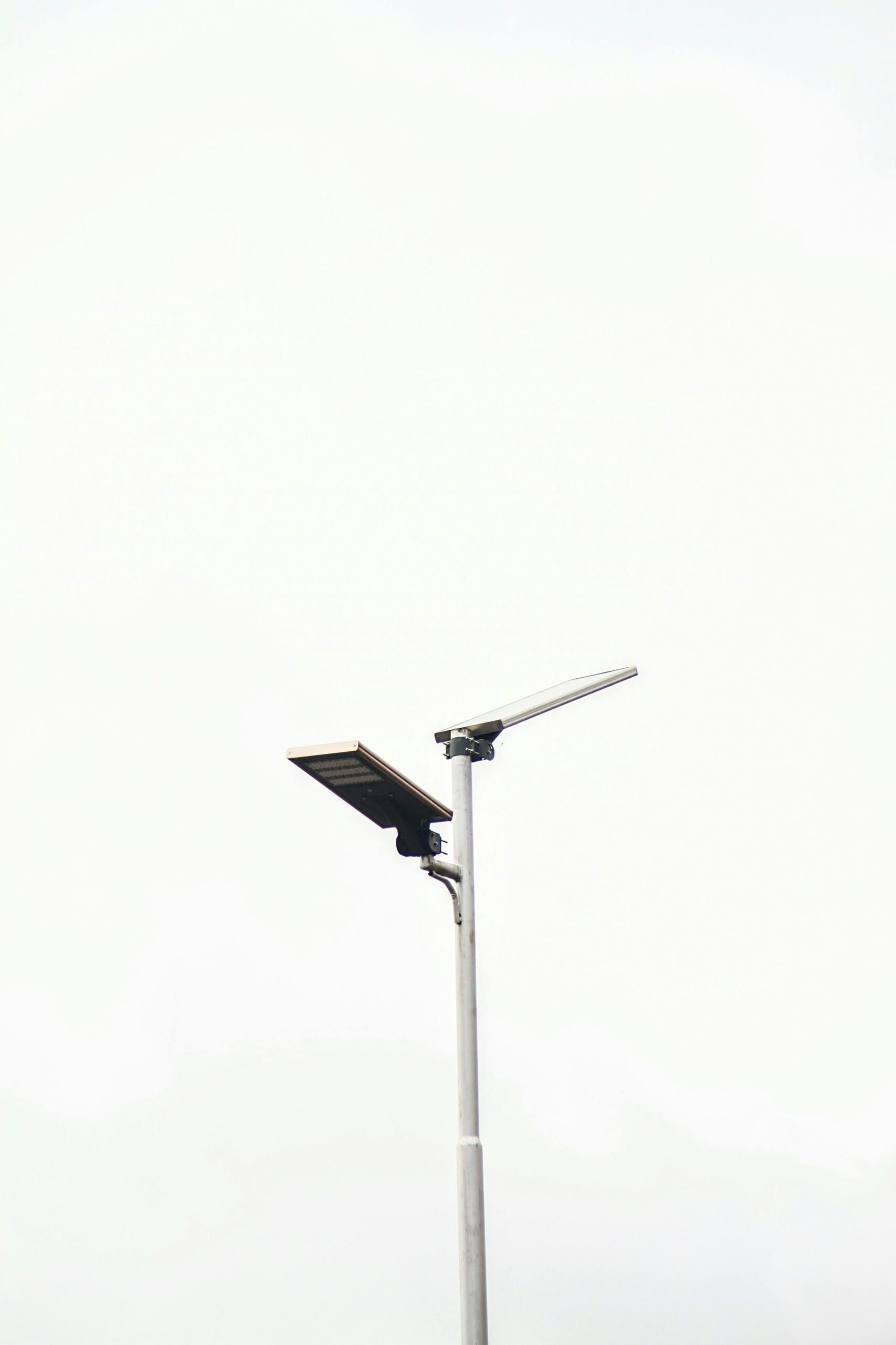 A minimalist solar-powered street lamp stands against a clear pale sky, emphasizing sustainability.